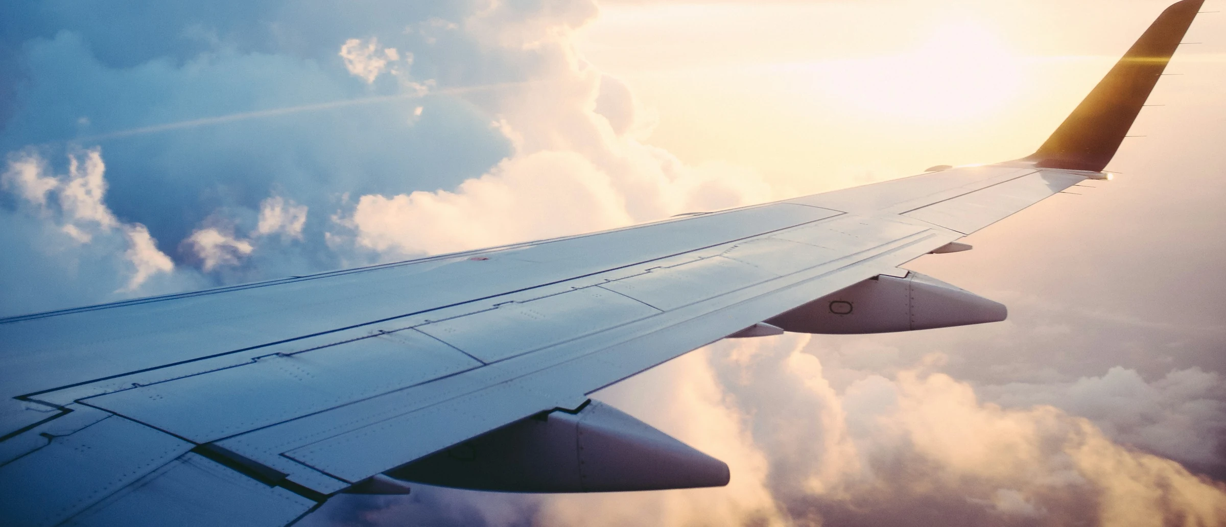 An aircraft wing and winglet above a bank of cloud in low sun.